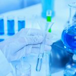 Flask in scientist hand with test tubes for analysis.